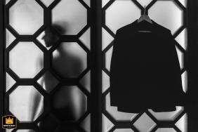 Black and white detail shot in Aix-en-Provence showing the silhouette of the groom behind the window with his jacket hanging nearby.